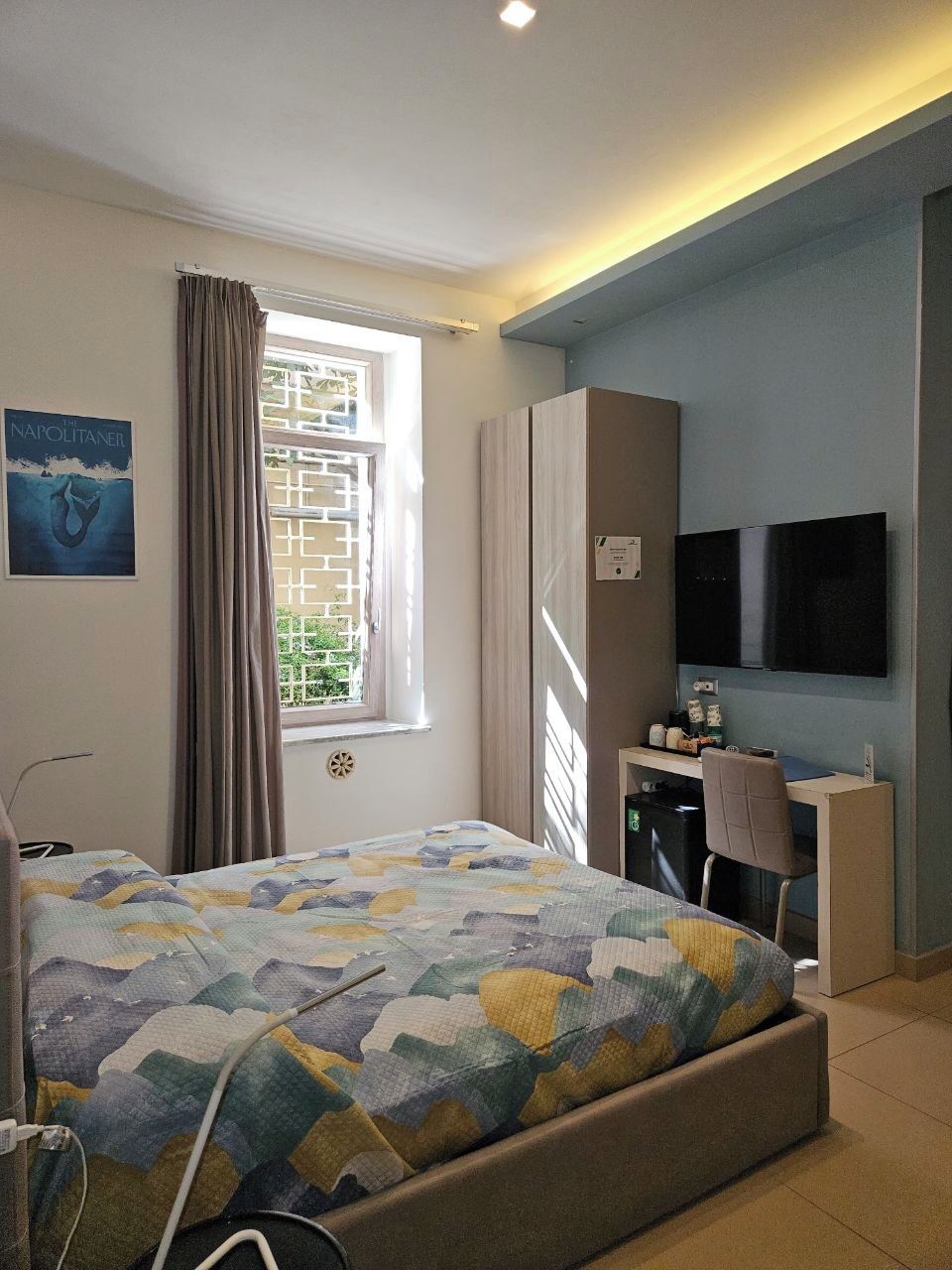 A bedroom with a bed, a desk, a television, and a window with curtains.