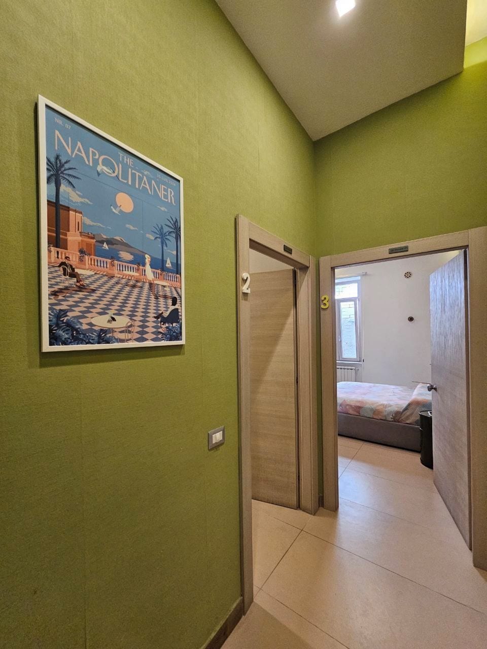 Ein Flur mit einem Strandplakat, einer Tür mit der Nummer 2 und einer Tür mit der Nummer 3, die zu einem Schlafzimmer führen.