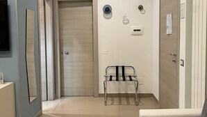 Habitación de hotel con cama, mesita de noche, silla, pequeña mesa, espejo y puerta.