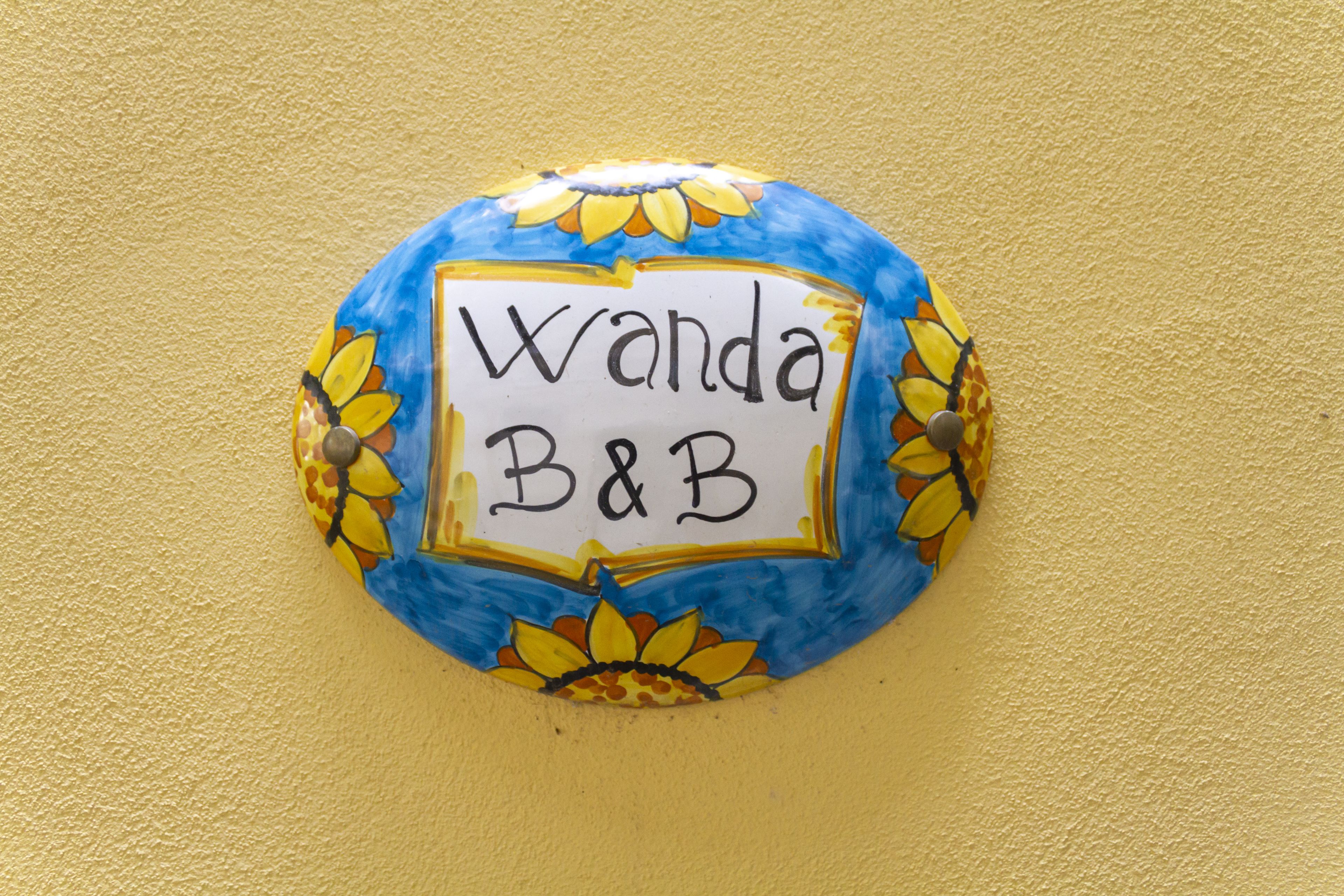 Un panneau rond et coloré, sur lequel on peut lire « Wanda B&B », est fixé à un mur jaune.
