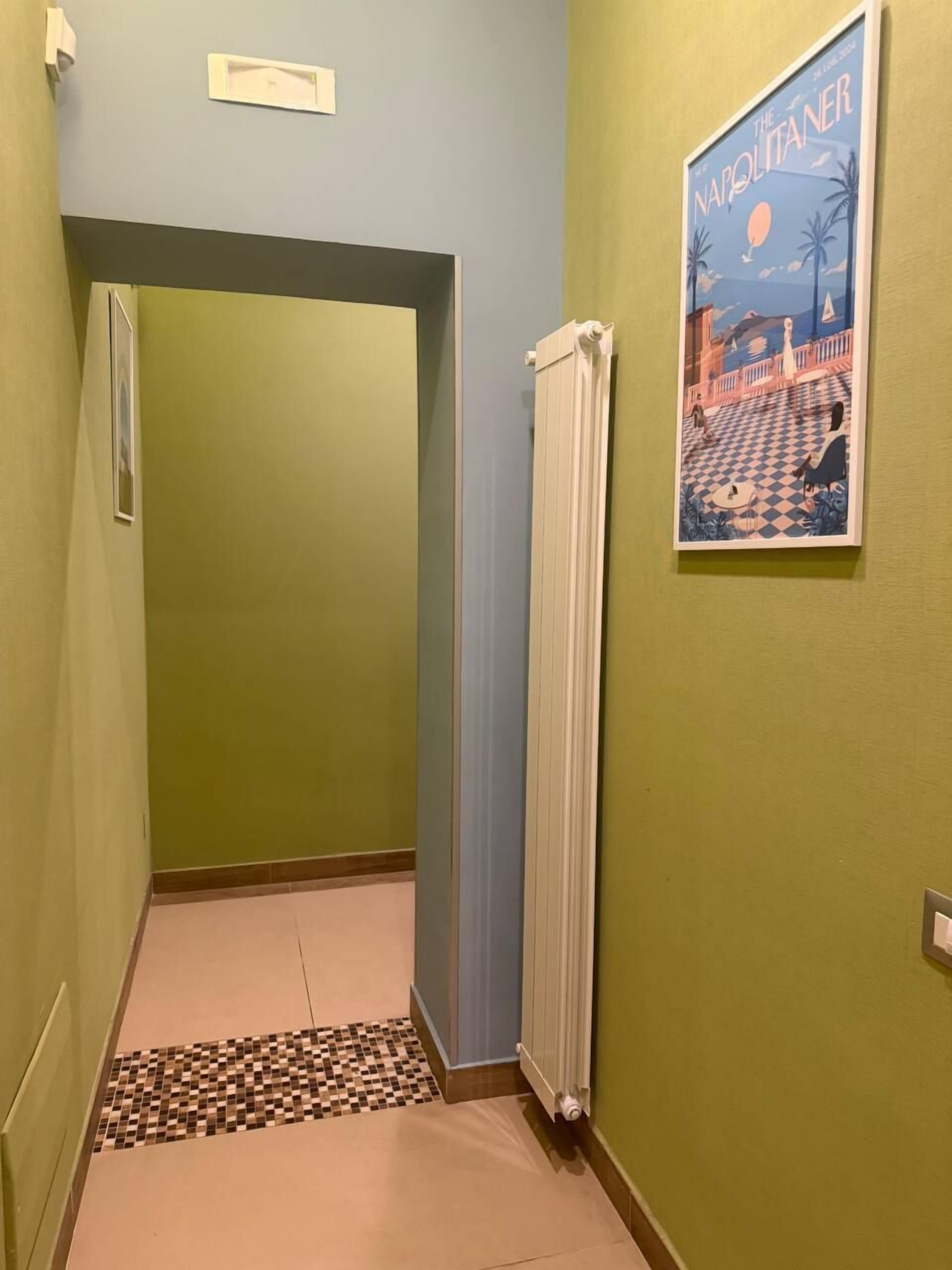 A narrow hallway with a radiator, a checkered floor mat, and a poster on the wall.