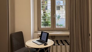 Un dormitorio con cama, un escritorio con una computadora portátil, una silla y una ventana con cortinas.