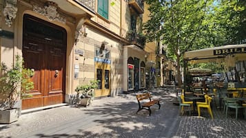 Une rue pavée avec un café, un banc et un bâtiment doté d’une grande porte en bois et d’une enseigne sur laquelle on peut lire « BRILLO ».