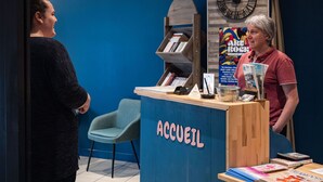 A reception desk with a sign reading 'ACCUEIL,' a blue wall, a clock, and a poster. - Hôtel du Champ de Mars (Saint-Brieuc)