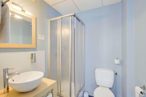 A bathroom with a white sink, mirror, and toilet, a glass shower enclosure, and a towel rack. - Hôtel du Champ de Mars (Saint-Brieuc)