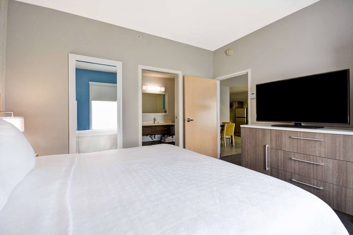 A hotel room with a large bed, a television, and a bathroom with a mirror and sink.