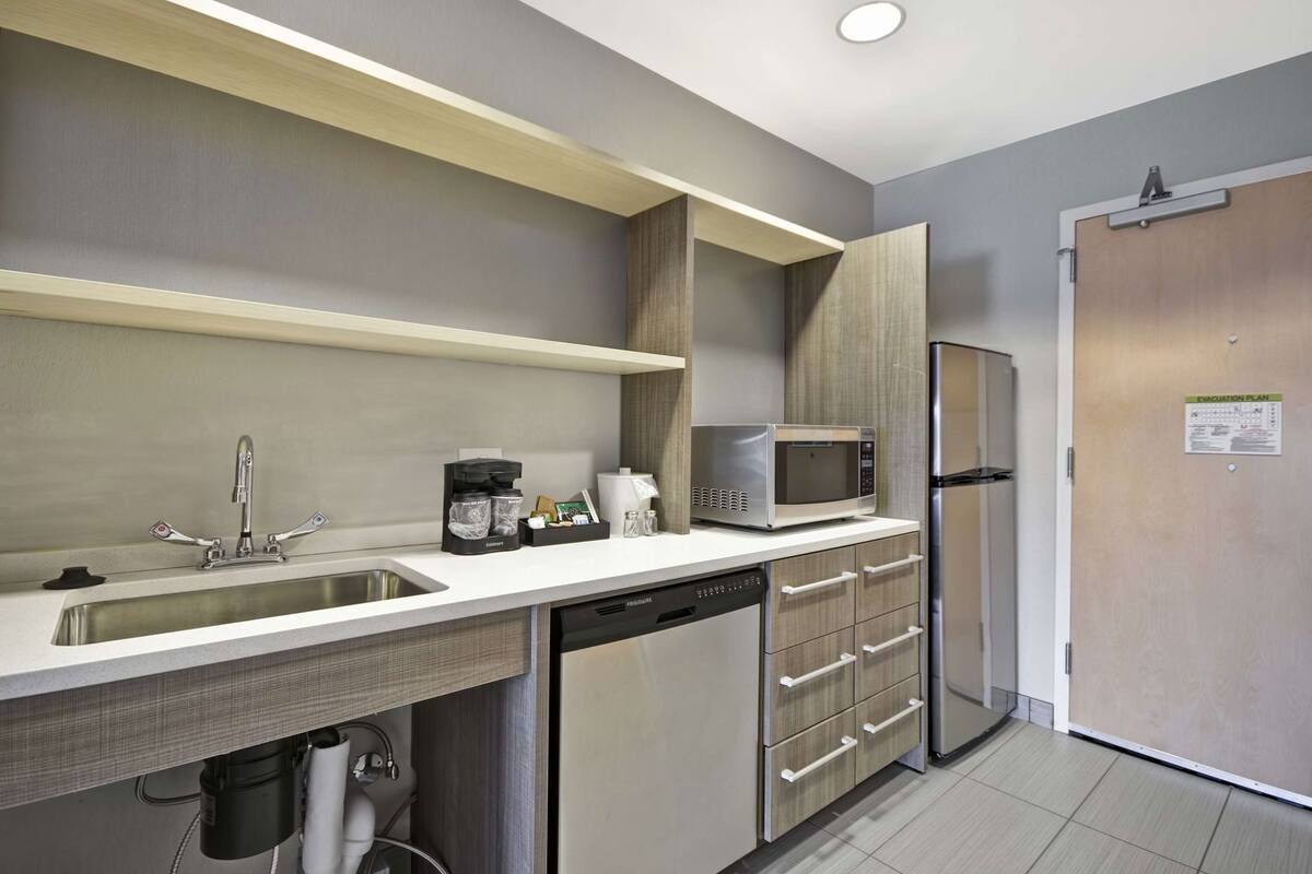 A modern kitchen with a stainless steel sink, a coffee maker, a microwave, and a refrigerator.