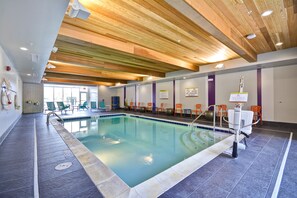 An indoor swimming pool with a wooden ceiling, tiled floor, and orange chairs around the pool.