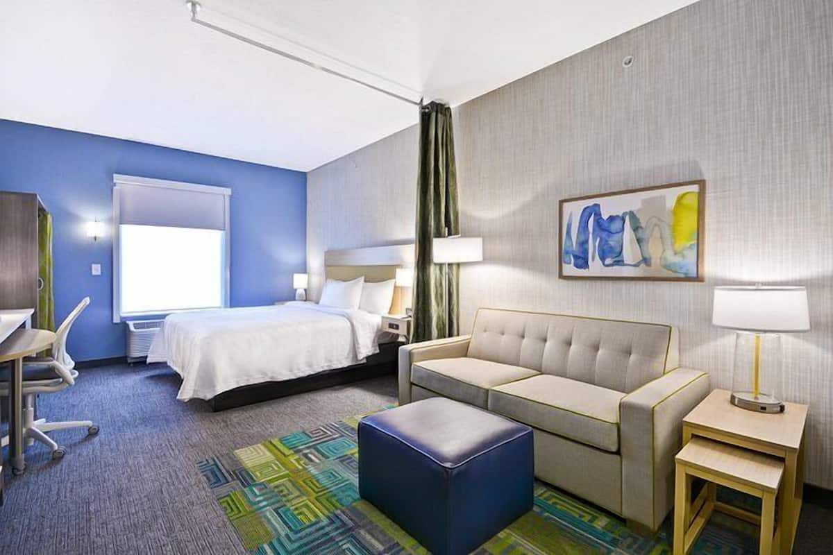A hotel room with a bed, a sofa, a desk, and a chair.