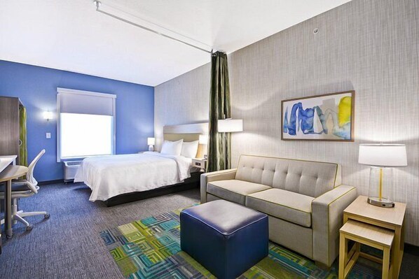 A hotel room with a bed, a sofa, a desk, and a chair.