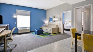 A hotel room with a blue accent wall, a sofa, a bed, a desk, and a dining area.