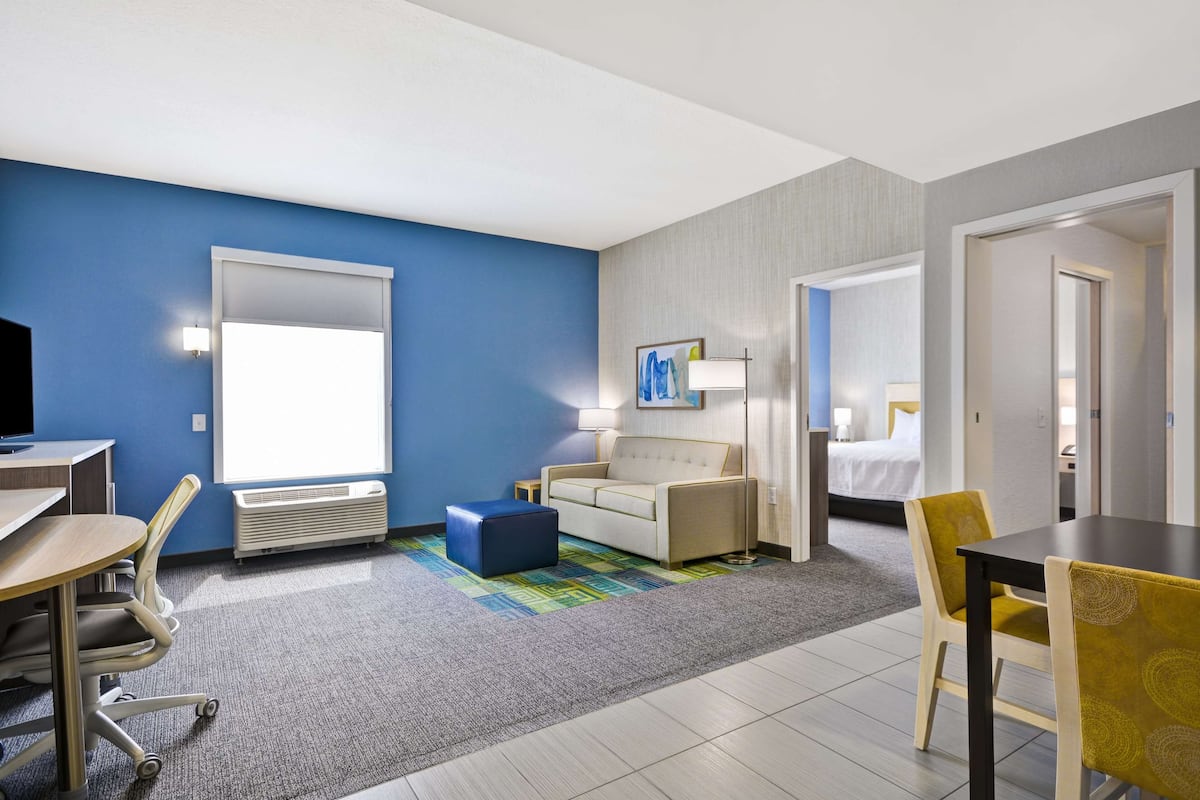 A hotel room with a blue accent wall, a sofa, a bed, a desk, and a dining area.