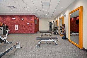 A gym with exercise equipment, a clock, and a mirror on the wall.