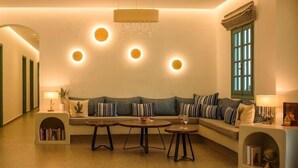 A modern living room with a sofa, two side tables, a bookshelf, and a chandelier. - Hotel Armonia (Santorini)