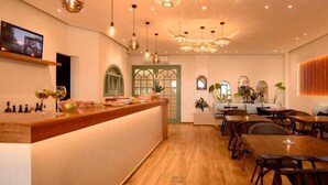 A restaurant interior with a wooden bar, dining tables, and hanging light fixtures. - Hotel Armonia (Santorini)