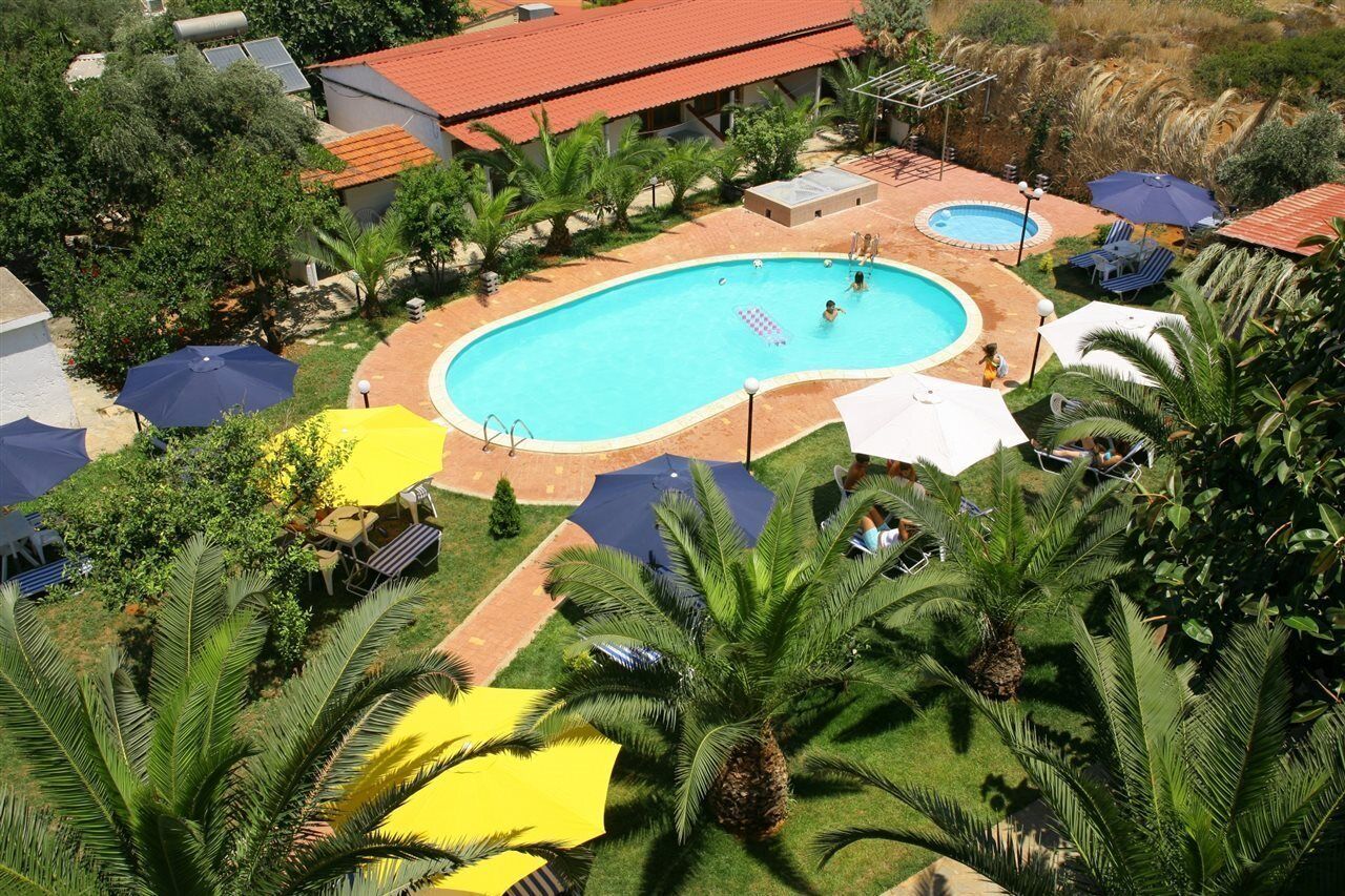 An aerial view of a resort with a large swimming pool surrounded by palm trees and umbrellas.