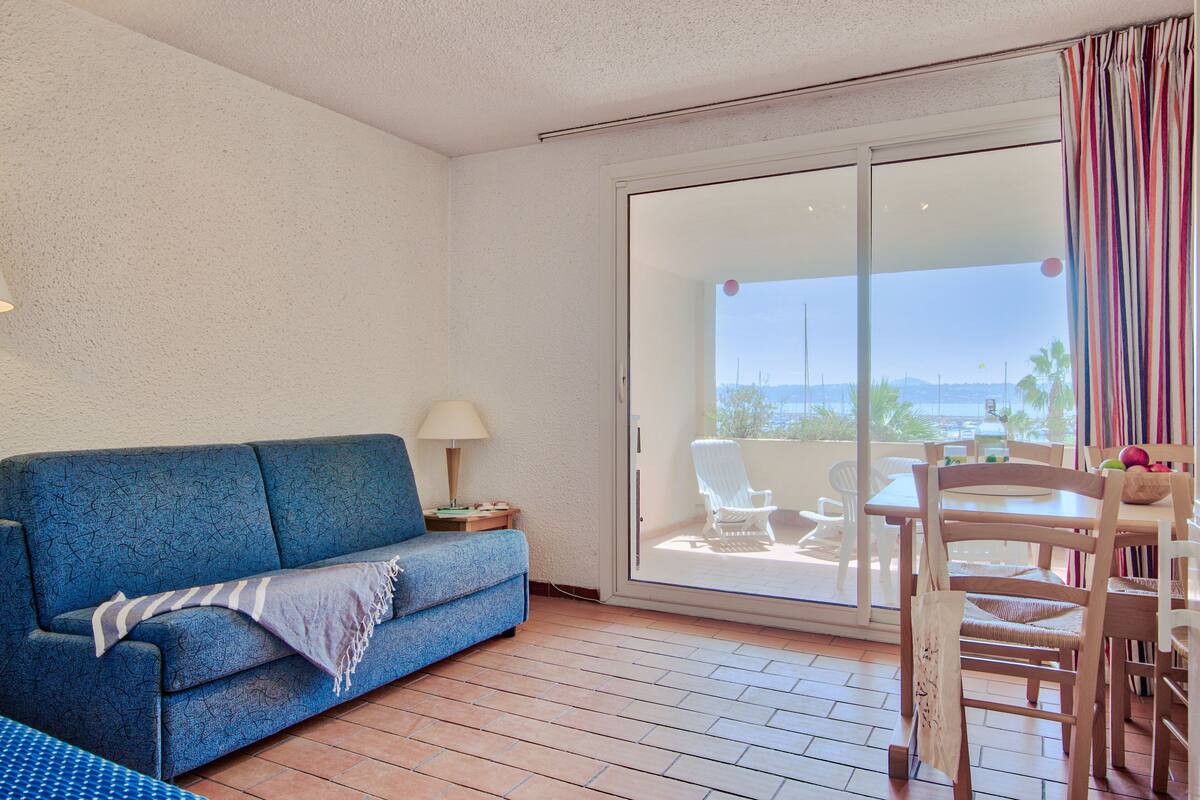 Une pièce avec un canapé bleu, une petite table avec une lampe, une table à manger avec des chaises et une porte-fenêtre coulissante donnant sur un espace extérieur avec vue sur la mer.