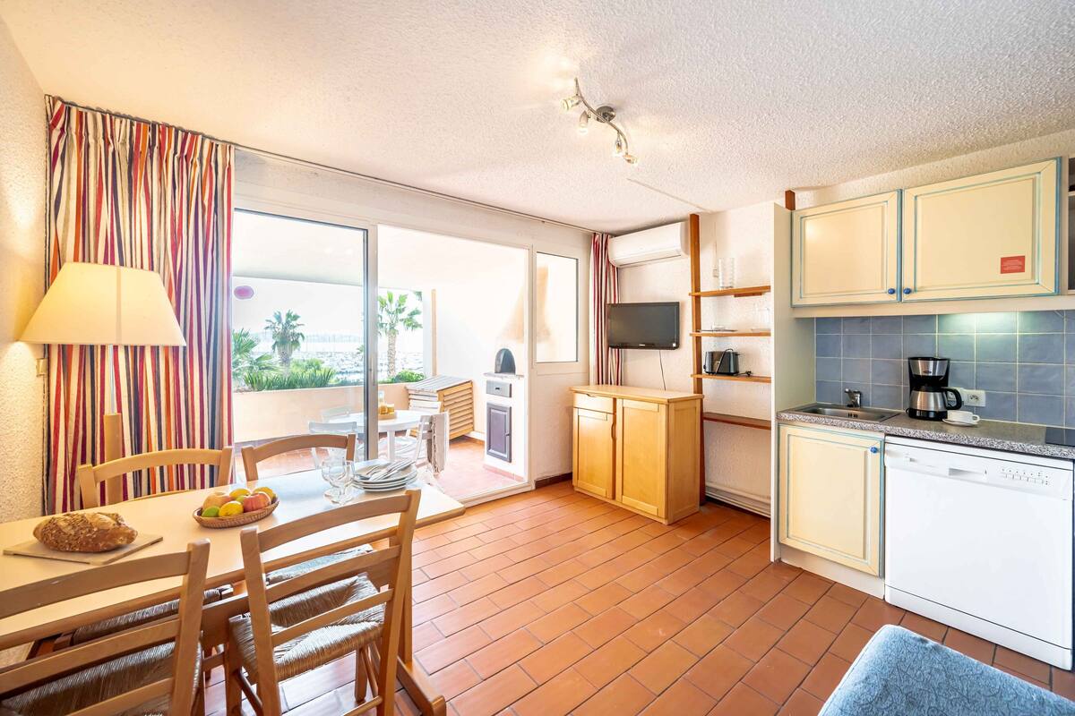 Une cuisine compacte avec un coin repas, un téléviseur et une vue sur l’extérieur.