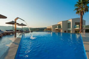 A swimming pool with lounge chairs and umbrellas, surrounded by modern buildings and a palm tree. - Hotel Porto Demo Boutique Adults Only (Corfu)