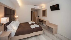 Habitación de hotel con cama, mesita de noche, lámpara, escritorio, silla y televisor de pantalla plana en la pared.