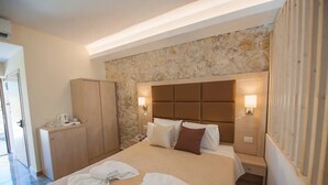 Habitación de hotel con una pared de acento de piedra, cama con ropa de cama blanca, dos lámparas de noche, armario de madera y una pequeña mesa con hervidor.