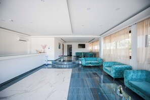 Un vestíbulo amplio con piso de mármol, una recepción y un área de descanso con sofás.