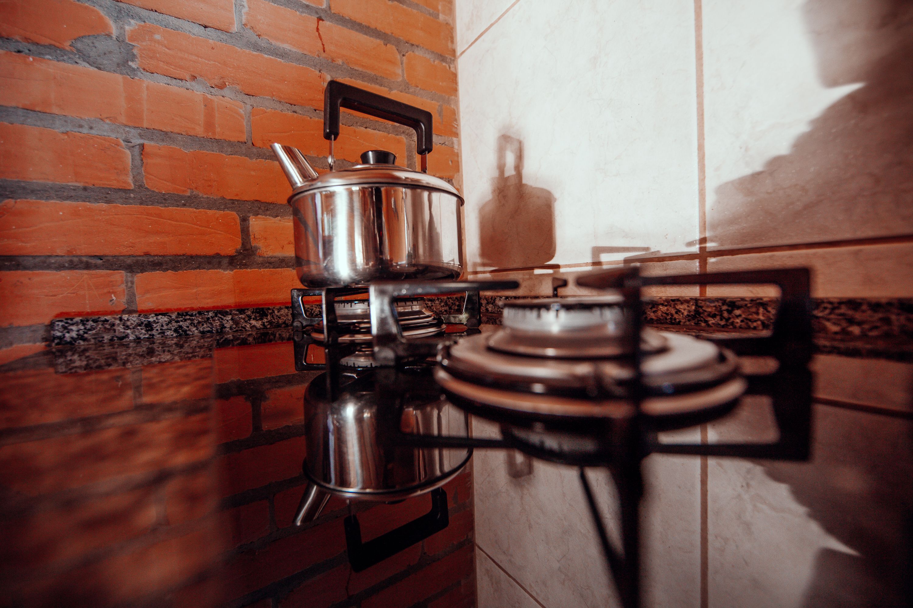 A kitchen with a gas stove, a pot on the stove, and a brick wall.