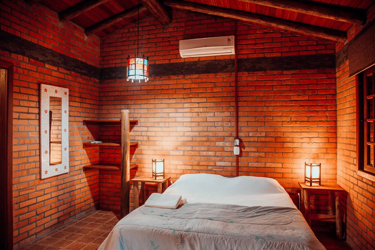 A room with a brick wall, a bed, a nightstand, and a hanging light fixture.