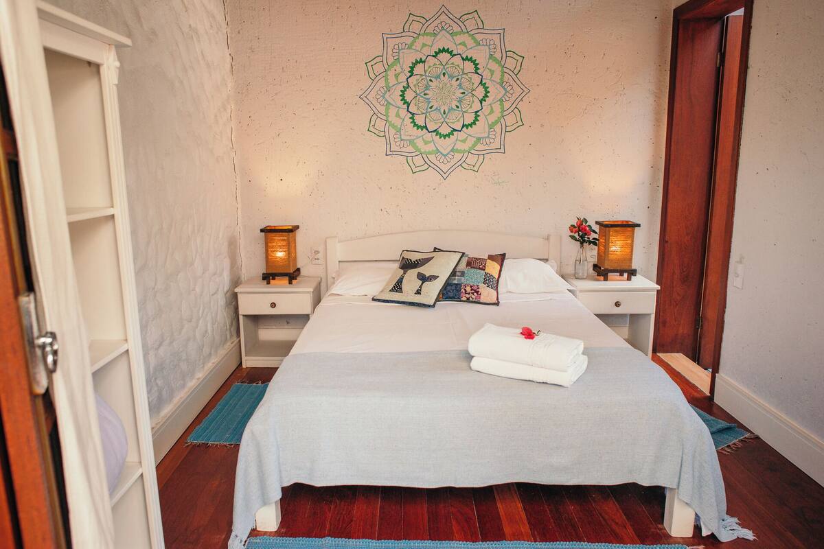 A neatly made bed with a white bedspread, two pillows, and a folded towel on a wooden floor.