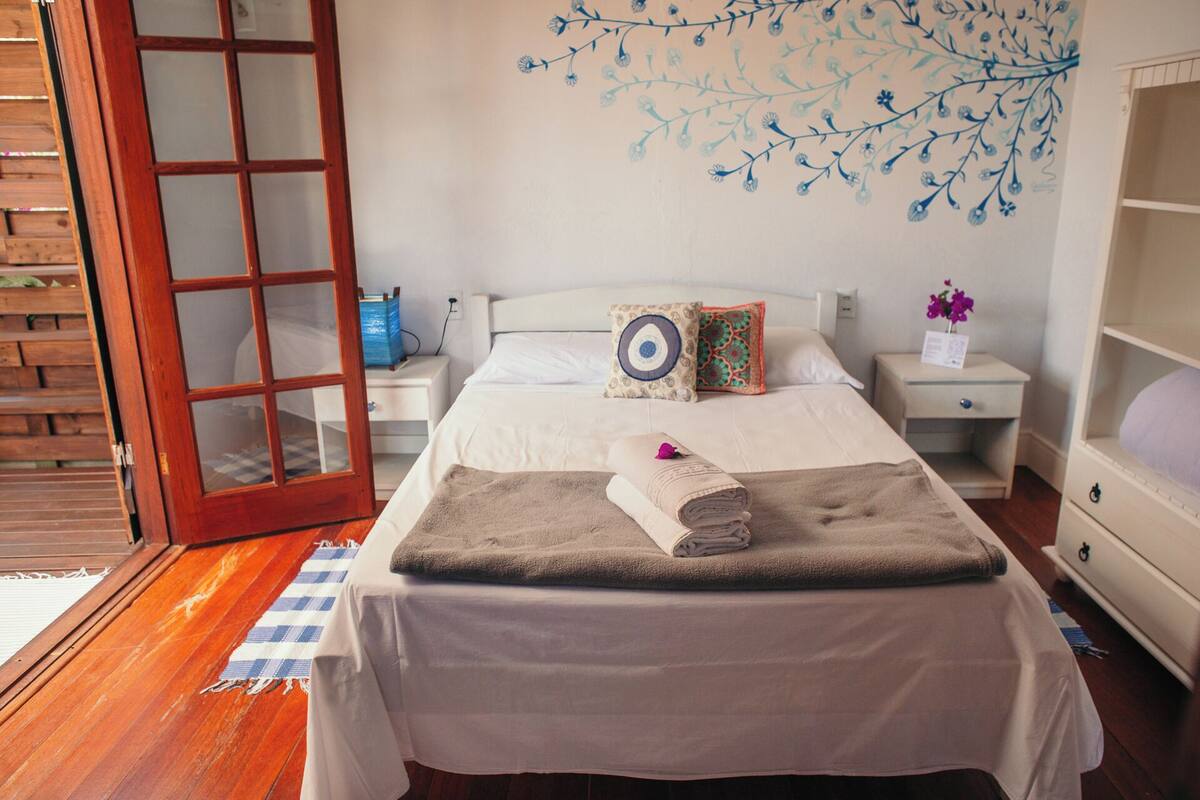 A bedroom with a bed, a nightstand, a dresser, a wooden door, and a wall with a floral pattern.