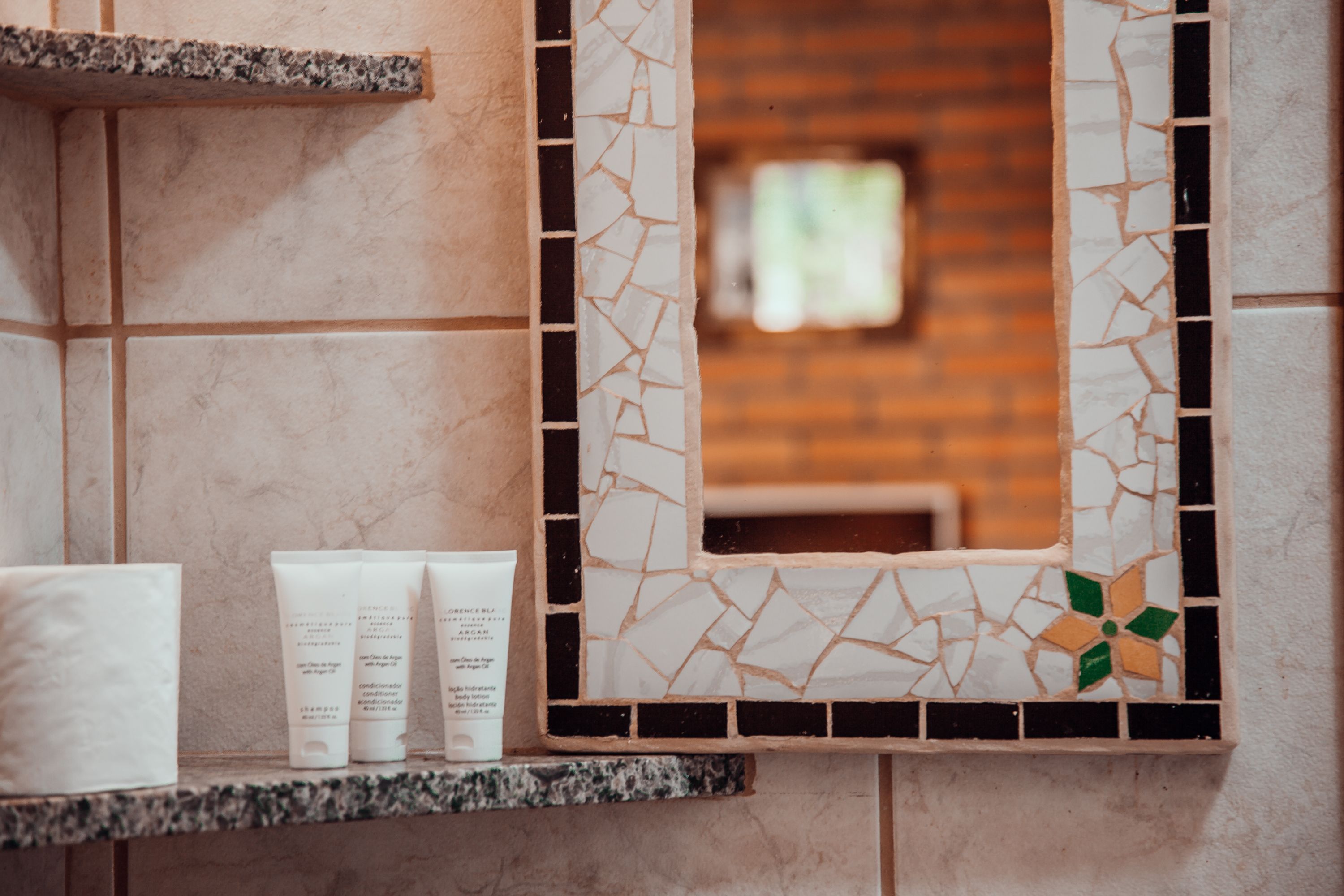 A bathroom with a tiled wall, a mirror, and toiletries on a shelf.