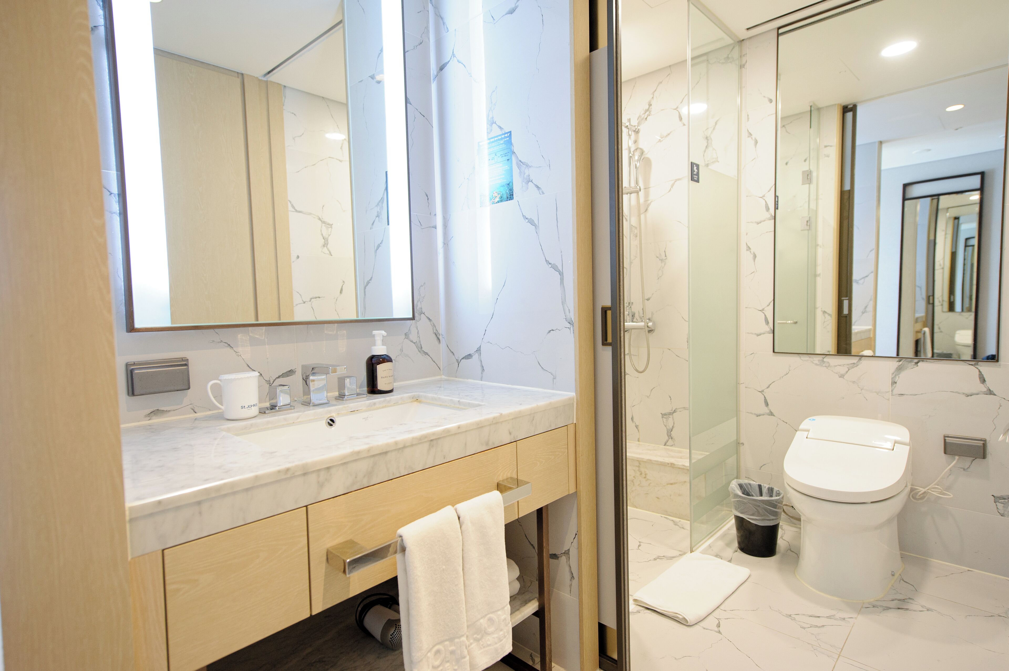 A modern bathroom with a marble countertop, a toilet, and a glass-enclosed shower.