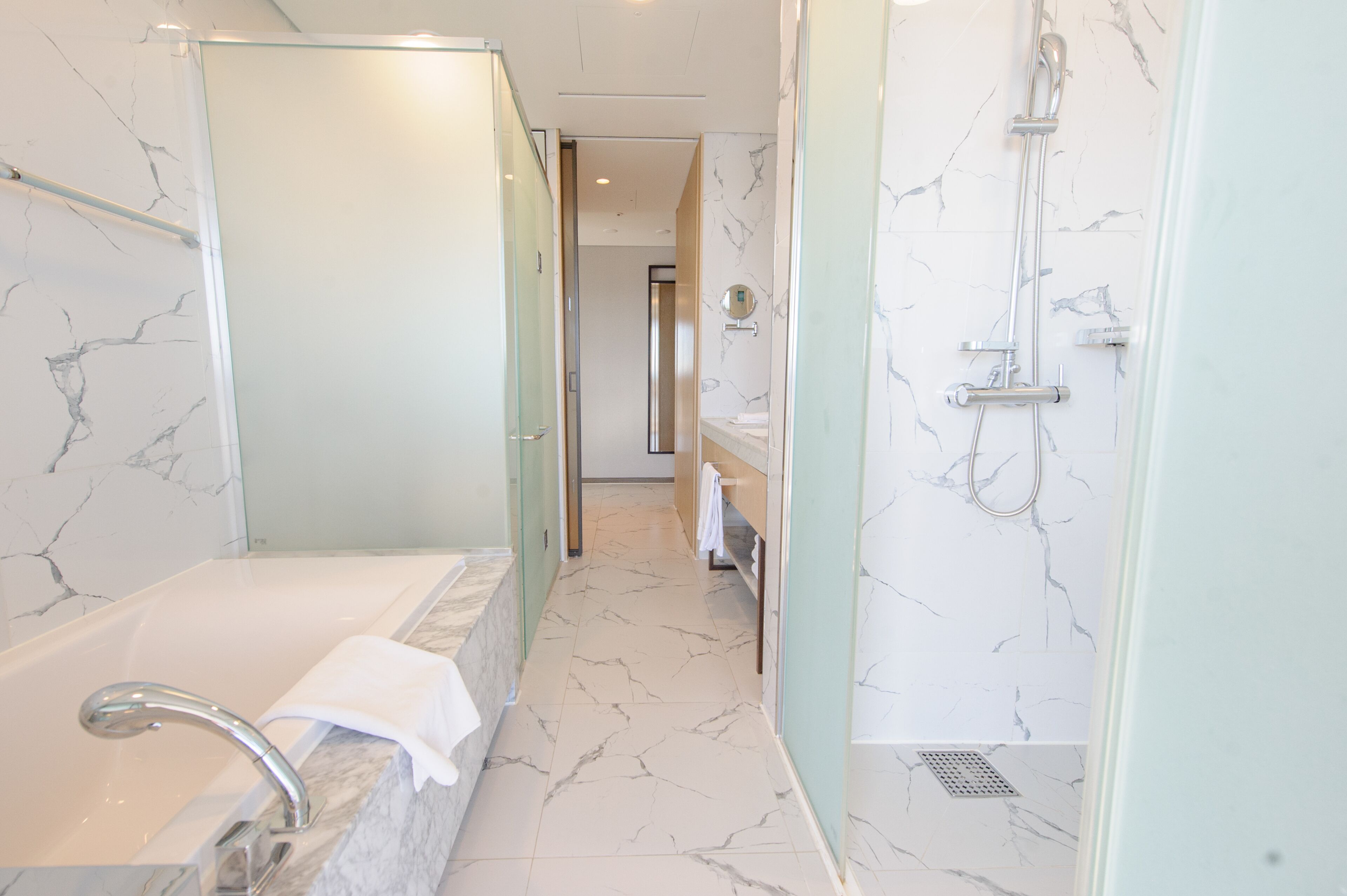Une salle de bain moderne avec un sol en marbre, une baignoire, une douche et des toilettes séparées par une paroi en verre.