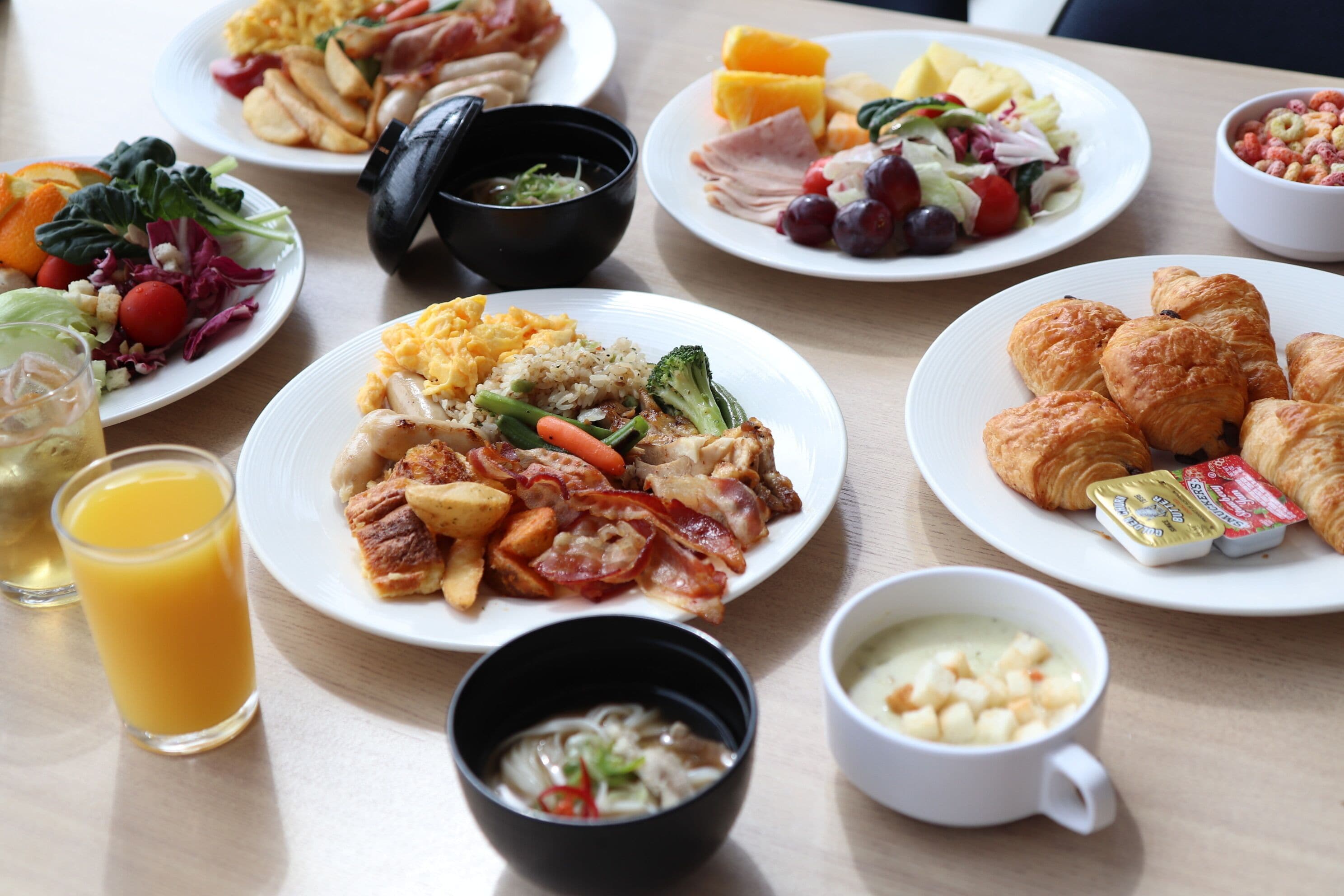 Una mesa con diferentes platillos de desayuno, como huevos, tocino y croissants.