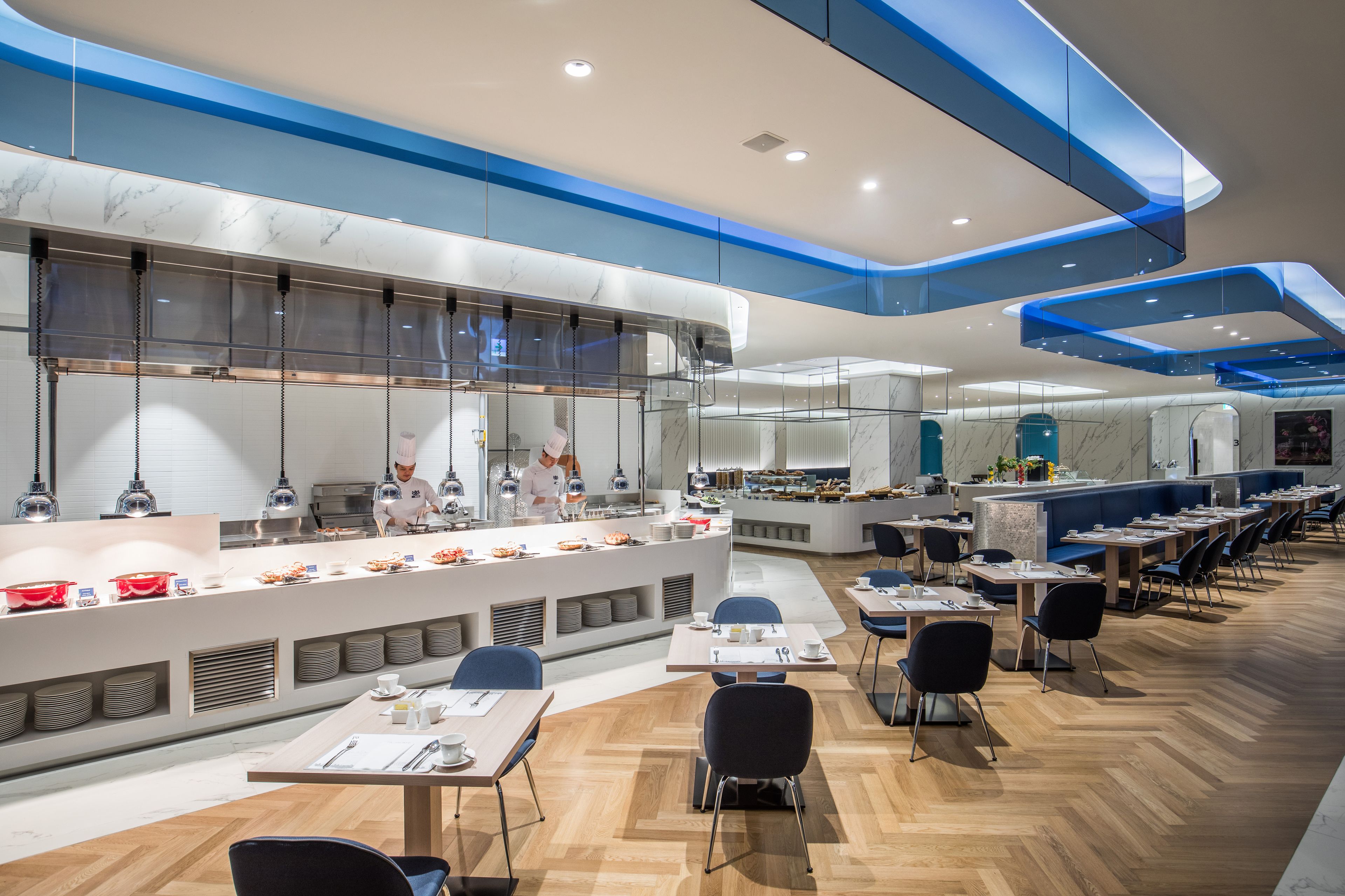 Un restaurante moderno con mostrador de mármol, detalles azules en el techo y mesas y sillas ordenadas.