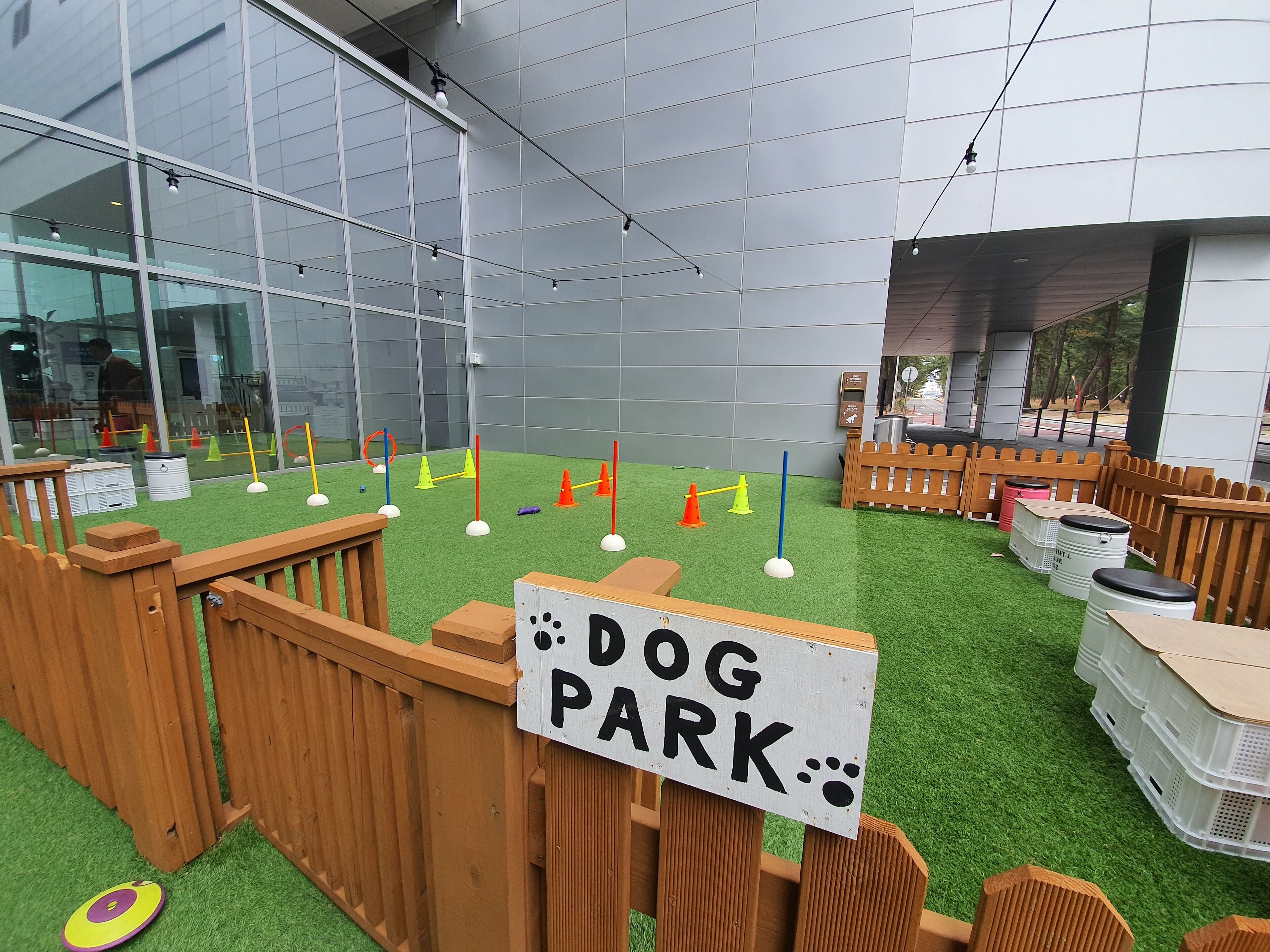 Un parc canin doté d’une clôture en bois, d’équipements d’agilité et d’un panneau indiquant sa fonction.
