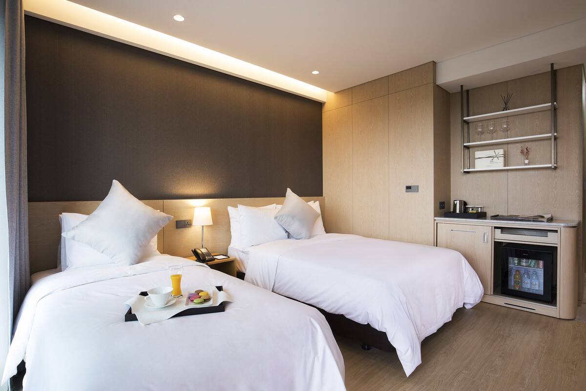 A hotel room with two beds, a minibar, and a small seating area.