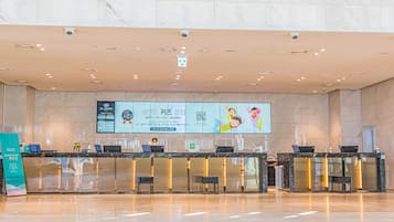 A modern reception area with marble walls and a polished floor. There are two reception desks with computers and seating. A large digital screen displays information and advertisements.