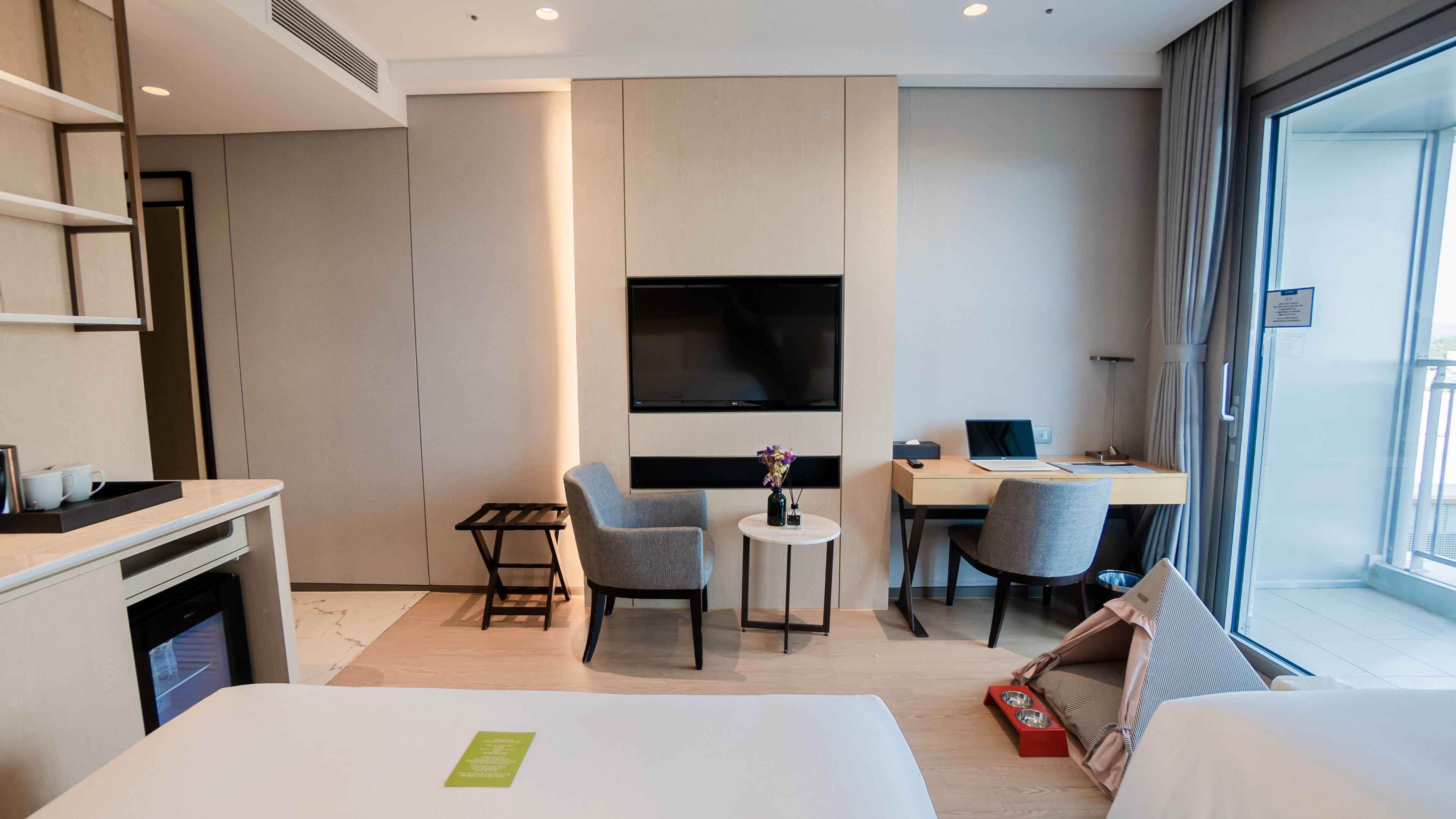 Quarto de hotel com cama, escrivaninha, cadeira, televisão e janela.