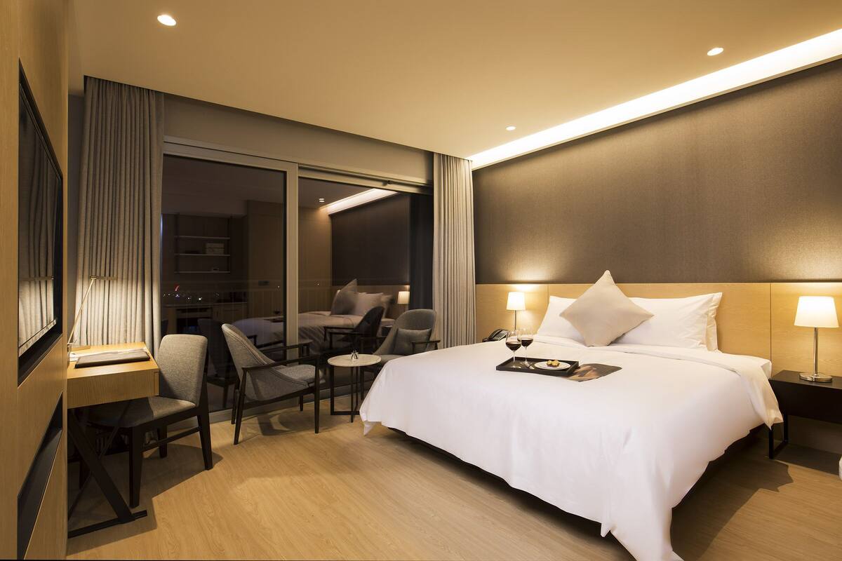 A modern hotel room with a large bed, a desk, and a seating area.