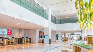 Een ruime lobby met een receptiebalie, zithoeken en een hoge plafond met hangplanten.