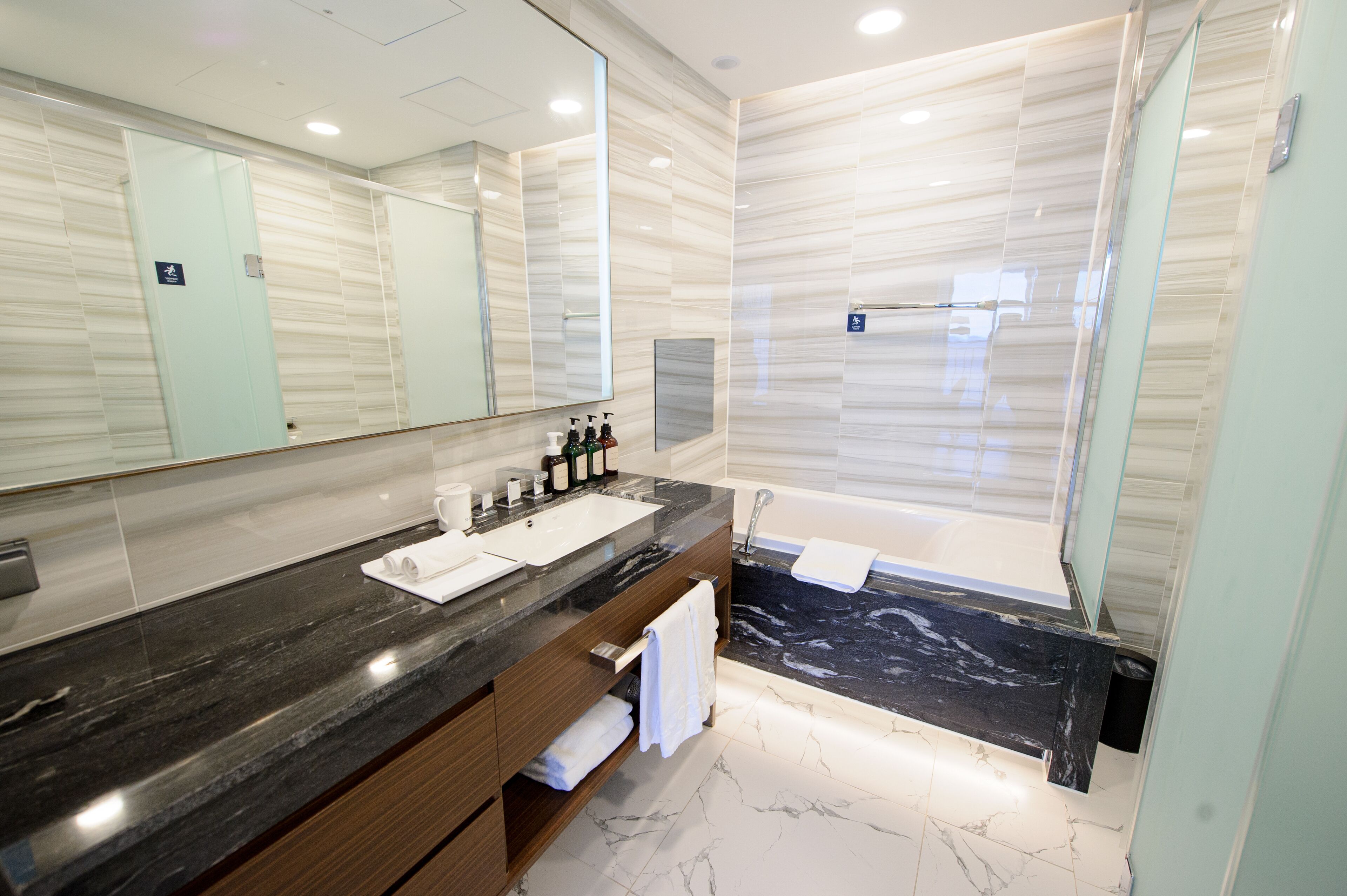 A modern bathroom with a marble vanity, a large mirror, a bathtub, and a shower area.