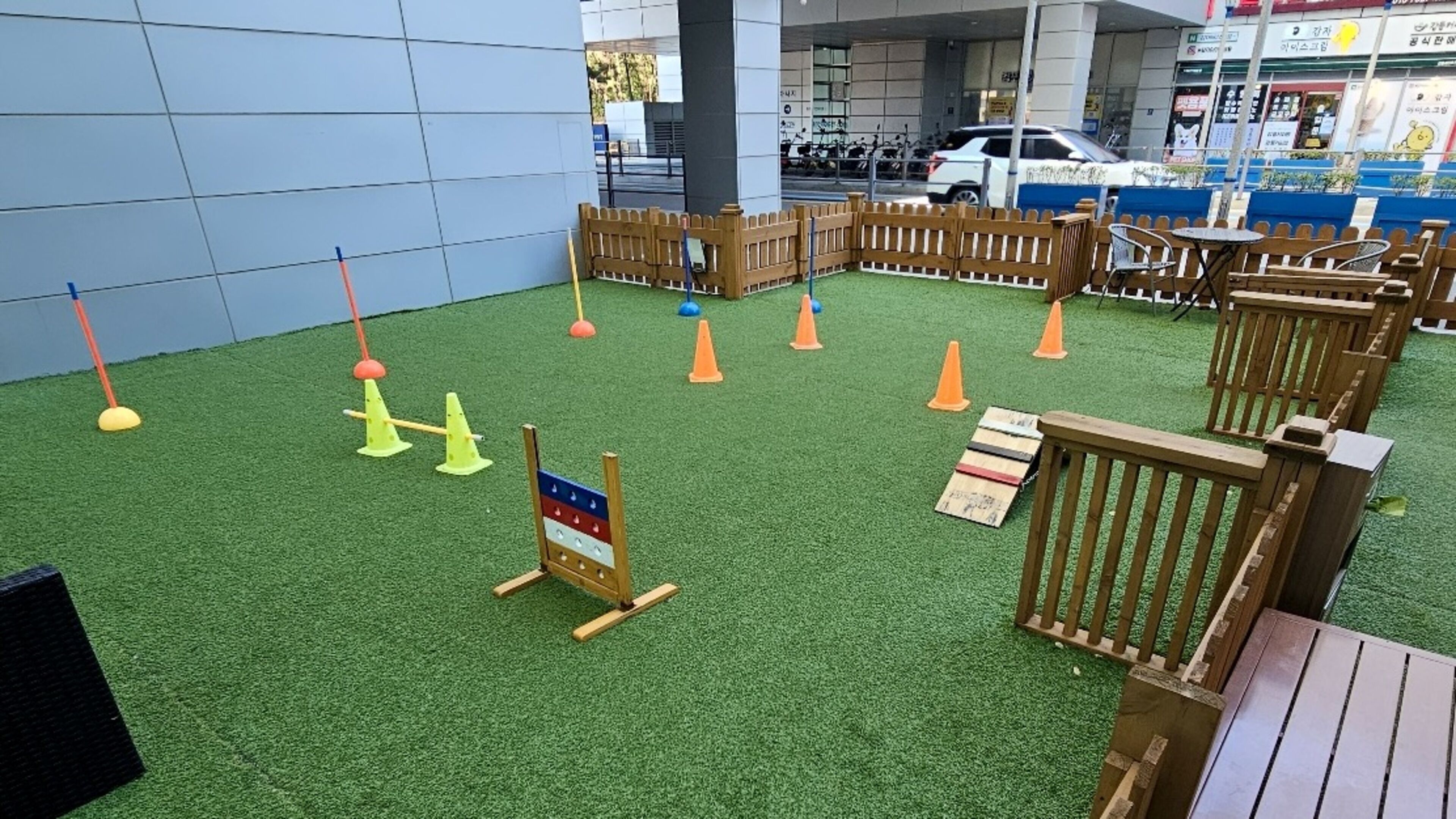A playground area with artificial grass, wooden play structures, and orange traffic cones.