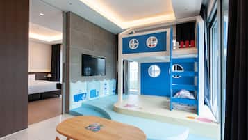 A modern hotel room with a large bed, a TV, a children's play area, and a dining table.