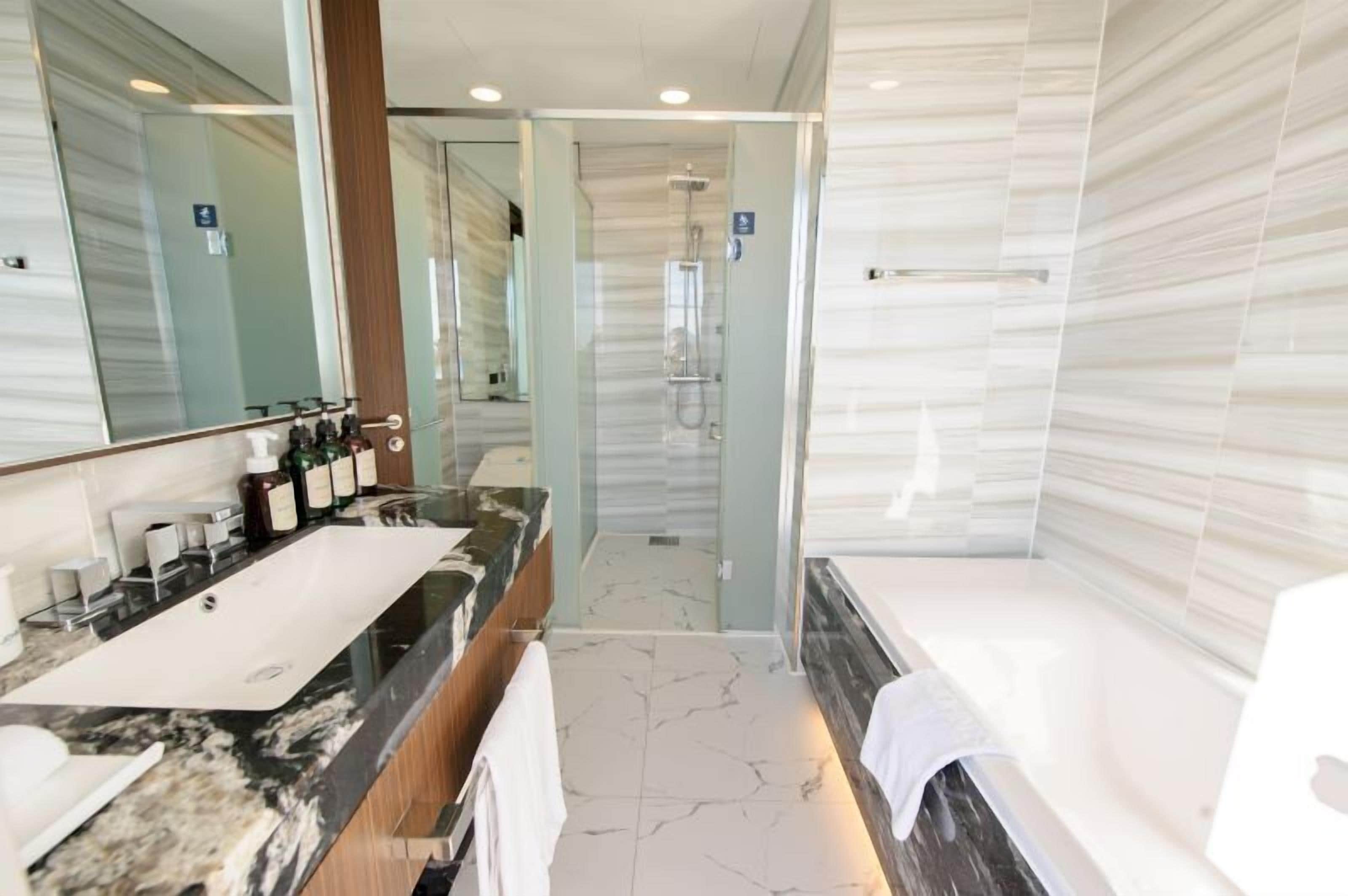 A modern bathroom with a marble sink, a large mirror, and a glass-enclosed shower.