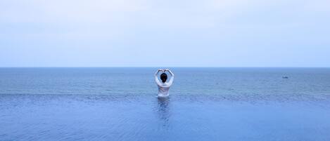 A person standing in calm sea water, making a heart shape with their hands.