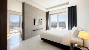 Een moderne hotelkamer met een groot bed, een flatscreen televisie aan de muur en uitzicht op de stad door grote ramen.