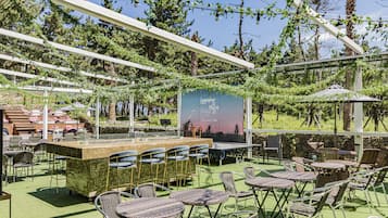 Un espace extérieur aménagé avec des tables et des chaises, un bar et un panneau d’affichage noir.