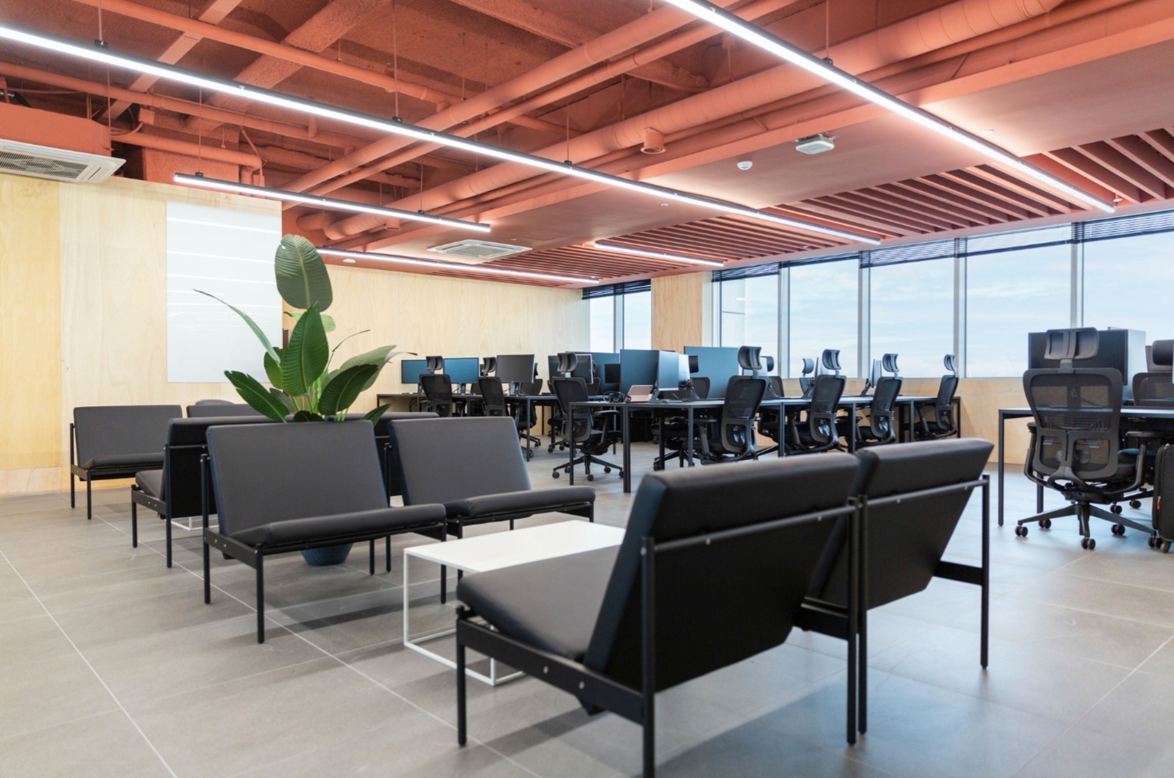 Een moderne kantoorruimte met rijen zwarte bureaustoelen, witte bureaus en grote ramen die voor natuurlijk licht zorgen.