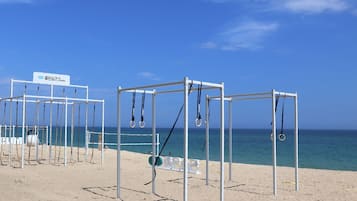 Outdoor gym equipment on a sandy beach with a clear sky and ocean in the background.